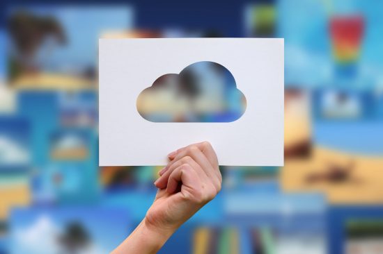 Hand holding a paper cutout of a cloud, symbolizing cloud backup services, with a blurred background of various digital images representing data protection and continuity.